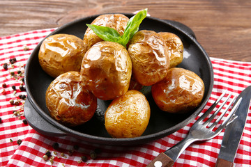 Baked potatoes in pan on checkered napkin on wooden table, closeup