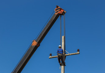 electrician install wire of the power line on electric power pole with crane.