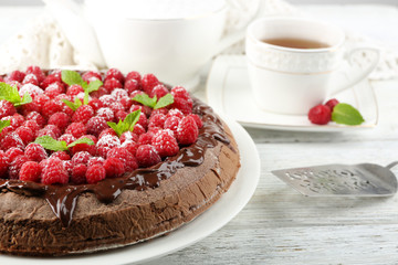 Cake with Chocolate Glaze and raspberries and cup of tea on color wooden background