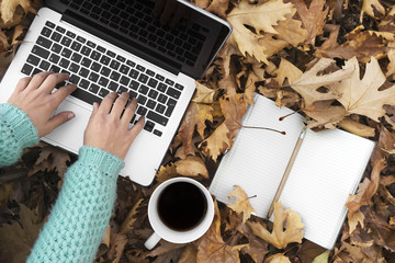 Woman sitting down in autumn leaves, using Laptop.