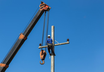 Electrician working on electric power pole with crane.