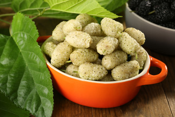 Ripe mulberries in bowls with green leaves on table close up