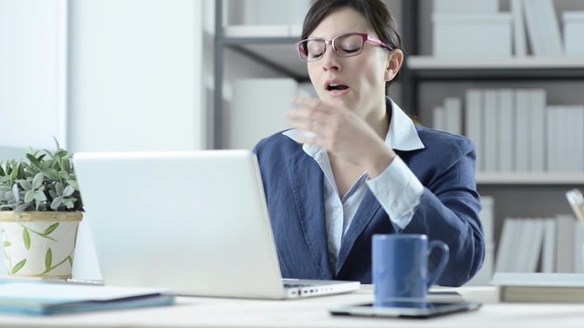 Bored businesswoman working at desk, yawning and taking off her glasses