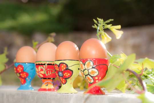 Row of four boiled eggs in colorful egg cups natural background
