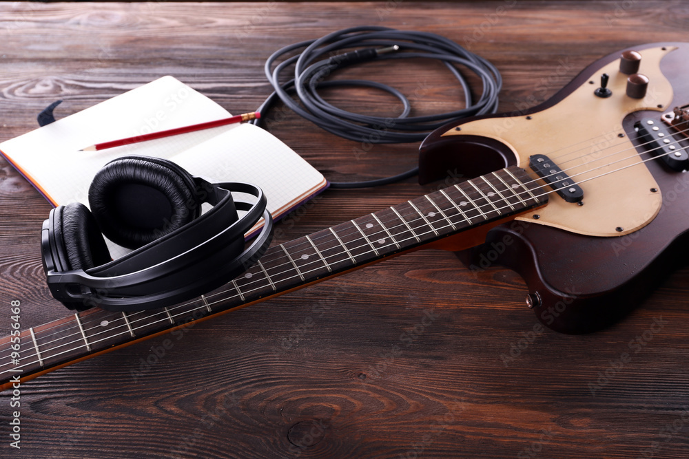 Sticker Electric guitar with headphones and notebook on wooden table close up