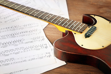 Plakat Electric guitar with music notes on wooden table close up
