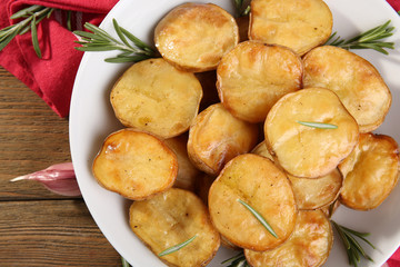 Delicious baked potato with rosemary in bowl on table close up