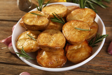 Delicious baked potato with rosemary in bowl on table close up