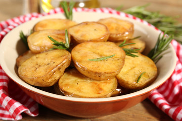 Delicious baked potato with rosemary in bowl on table close up
