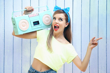 Beautiful girl with pretty smile holding retro tape recorder on color wooden background