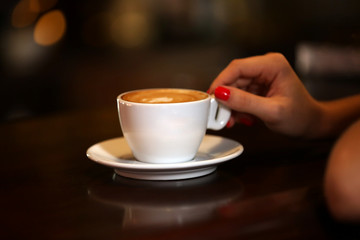 Female hand with cup of cappuccino on bar background