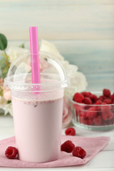 Plastic cup of milkshake on light wooden background