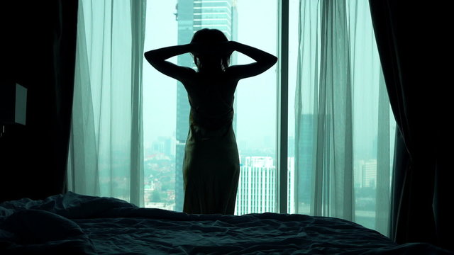 Young woman stretching her arms and admire view from window
