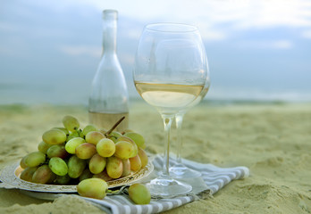 Romantic composition of white wine and grape on sandy beach