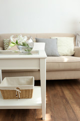 Pastel color sofa with beautiful pillows and vase with flowers on the table in front of it in the room