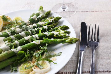 Appetizing asparagus in sour cream sauce with onion, cheese and lemon on the table, close up