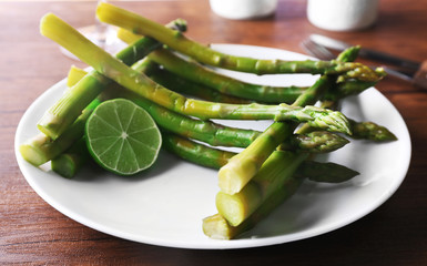 Fresh asparagus dish with lime on white plate against wooden background, close up