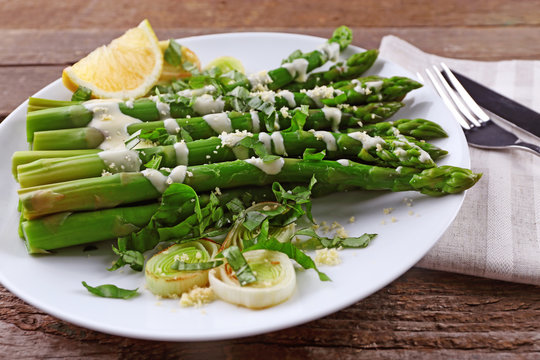 Fototapeta Appetizing asparagus in sour cream sauce with onion, cheese and lemon on white plate against wooden background, close up