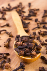 Heap of cloves with wooden spoon on table, seasoning for cooking