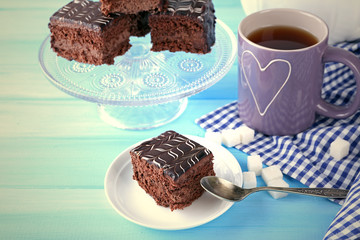 Served table with a cup of tea and chocolate cakes on blue background close-up