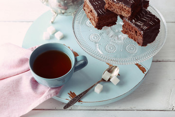 Served table with a teapot, a cup of tea and chocolate cakes on blue and whit background close-up