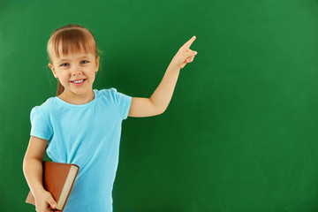 Beautiful little girl with book,  on blackboard background