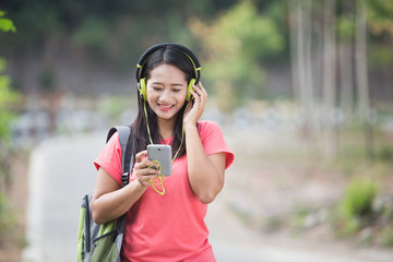 Fototapeta na wymiar Young Asian student in her outdoor activity, listening to the mu