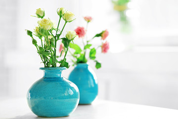 Beautiful roses in turquoise vases on window background