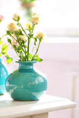 Beautiful roses in turquoise vases on window background