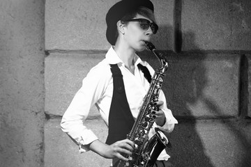 Girl with saxophone outside near the brick wall