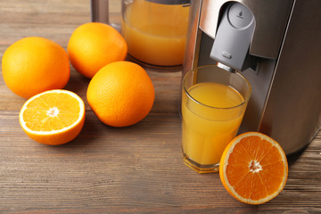 Stainless juice extractor with glass of orange juice on wooden background, close up