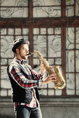 Young man plays saxophone on urban background