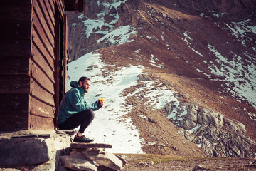 Man outside a mountain home drinking coffee