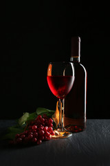 A bottle and a glass of wine, red grapes, on grey-black background