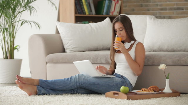 Beautiful girl sitting on floor with laptop and drinking juice