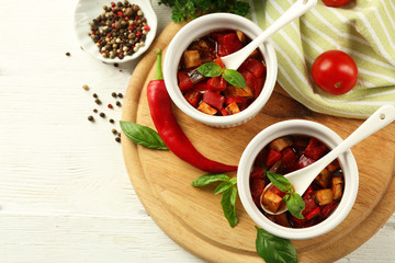 Tasty vegetarian ratatouille made of eggplants, squash, tomatoes in bowls on wooden table background
