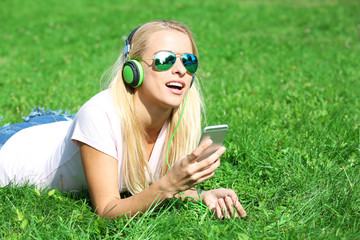 Young woman with earphones and smartphone listening to music on grass