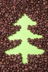 Coffee beans scattered on green paper with drawn christmas tree