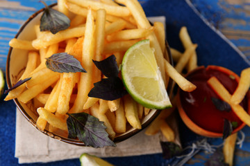 French fried potatoes in bowl with basil and sauce on old wooden background