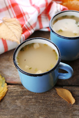 Two mugs of soup and napkin on wooden background