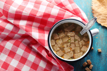 Mug of soup and napkin on blue wooden background