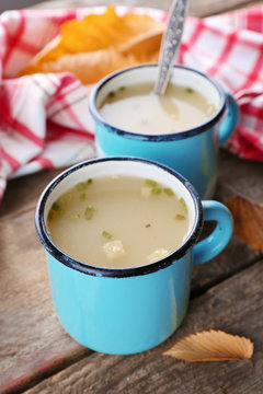 Two mugs of soup and napkin on wooden background