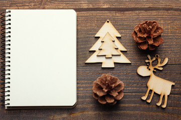 wooden tree decorations in the shape of Christmas tree and deer, together with a notebook on a brown wooden background