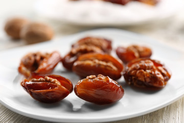 Walnut and date fruit in plate on wooden table, close-up