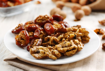 Walnut and date fruit in plate on wooden table, close-up