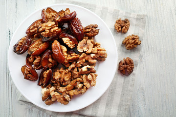 Walnut and date fruit in plate on wooden table, close-up