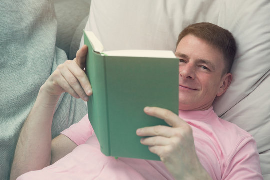 man lying on couch and reading a book