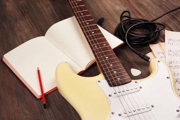 Fototapeta premium Electric guitar with musical notes and cord on wooden background
