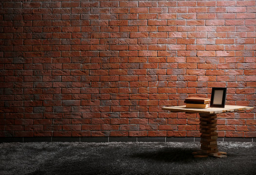 Small Wooden Table, Books And A Photo Frame On Red Brick Wall Background