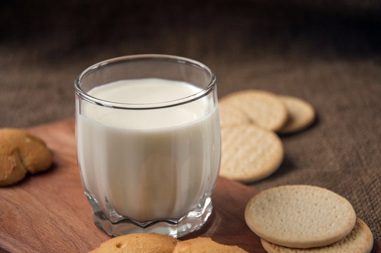 A glass of milk with cookies on a wooden board on a background sacking, burlap,